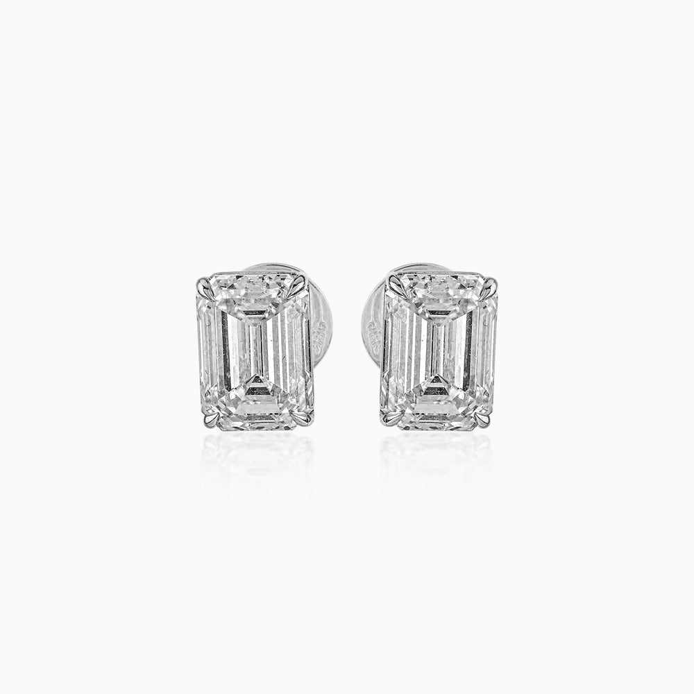 Emerald-cut diamond stud earrings in white gold, reflecting light on white background