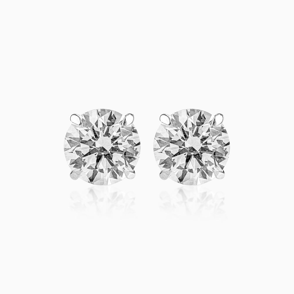 Two brilliant-cut diamond stud earrings against a white background, reflecting light.