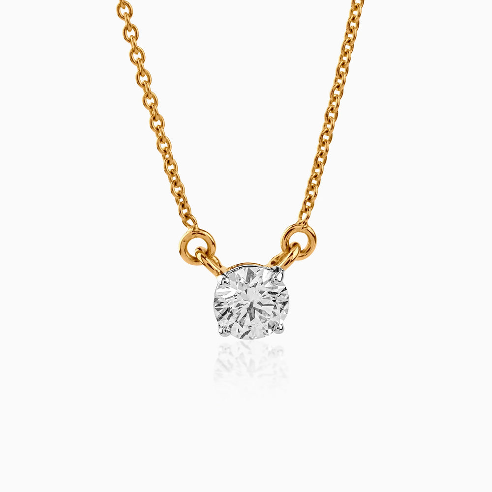 Delicate gold necklace with solitaire round diamond pendant, sparkling against white background