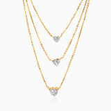 Gold layered necklace with three heart-shaped diamond pendants on delicate chains.