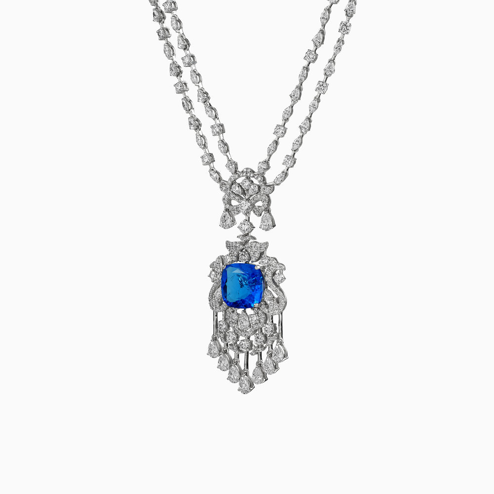 Intricate diamond necklace with vibrant blue sapphire pendant, draped elegantly against white background.