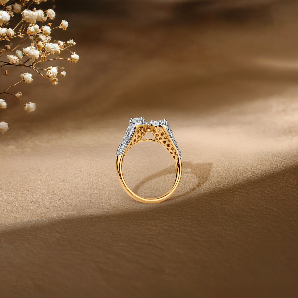 Gold and diamond ring with intricate design, casting shadow on soft beige background with delicate white flowers.
